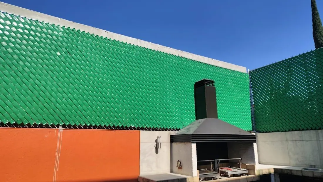 Malla con cinta de privacidad verde en una terraza con asador