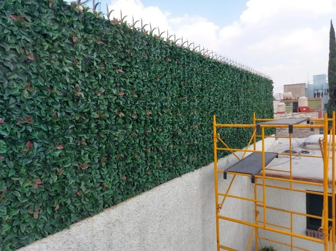 Instalación de follaje artificial sobre una barda, con andamio