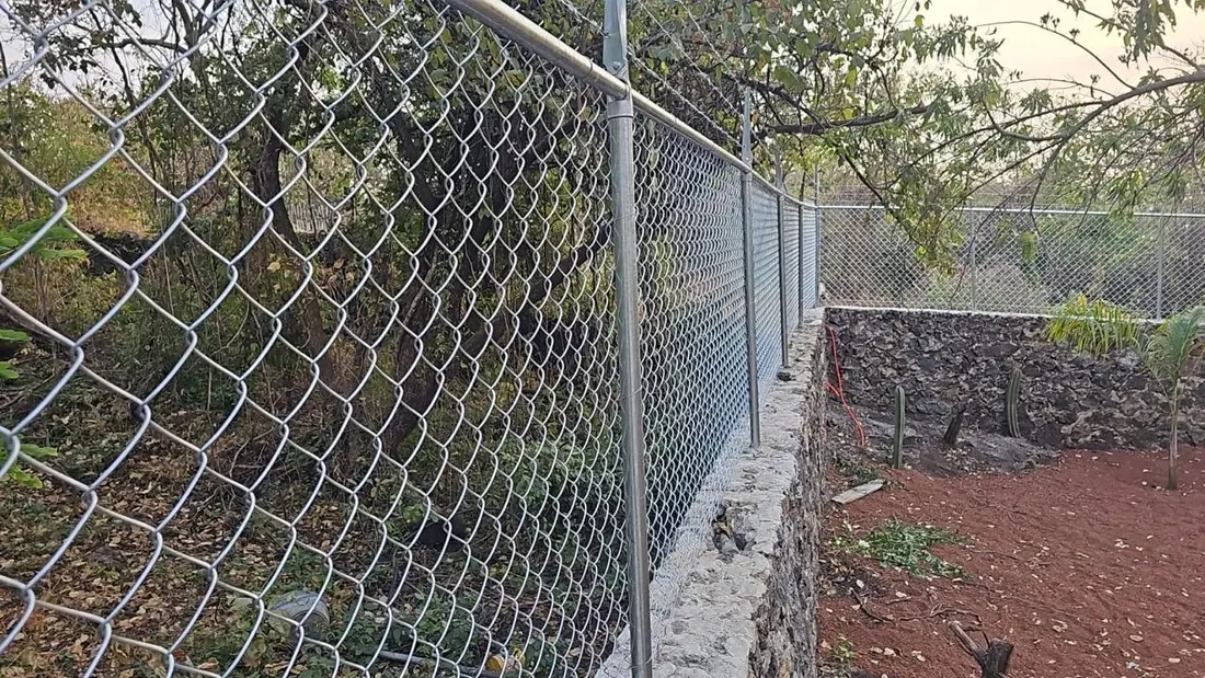 Malla ciclónica galvanizada instalada sobre un muro de piedra en un terreno residencial