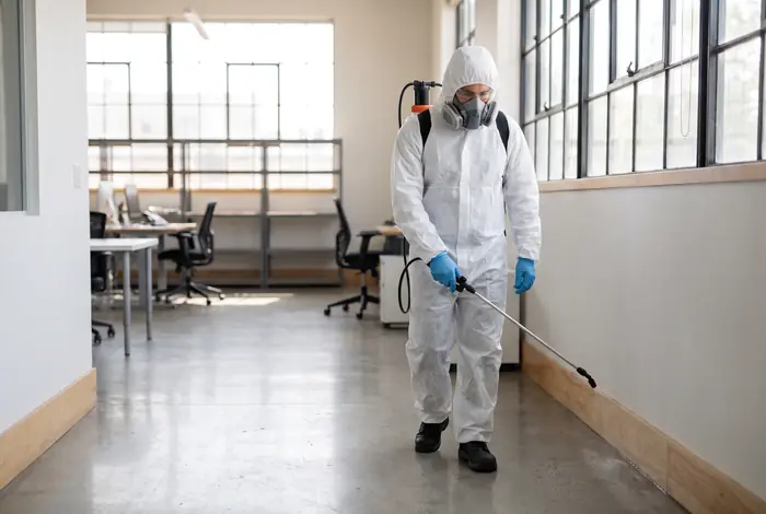 Técnico con traje de protección aplicando control de plagas en una oficina